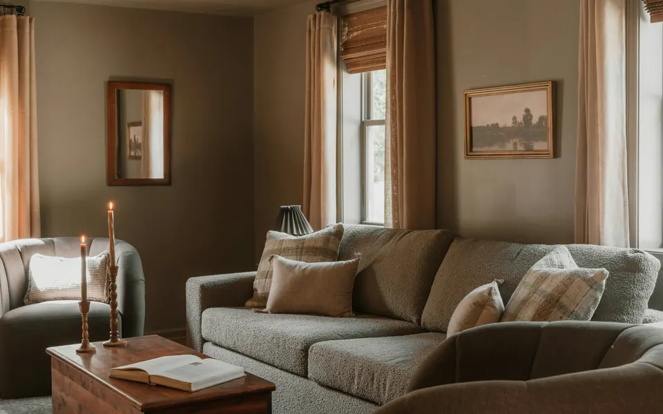 Wohnzimmer im warmen Nachmittagslicht mit Sofa, Kerzen und aufgeschlagenem Buch auf dem Couchtisch