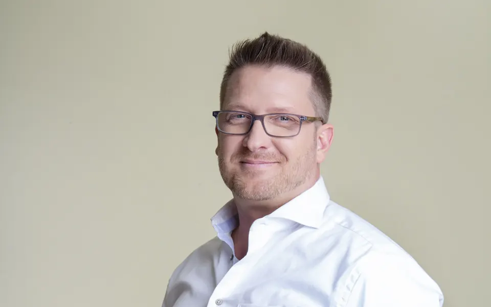 Andreas Pirker im weißen Hemd vor hellem Hintergrund, lächelnd