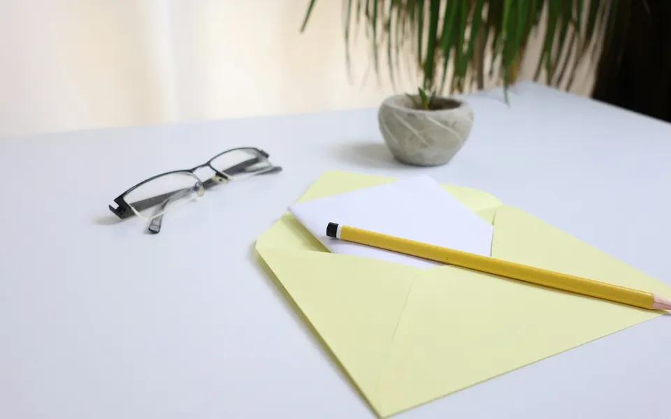 Brille, Bleistift und geöffnetes Kuvert mit Brief auf einem hellen Schreibtisch